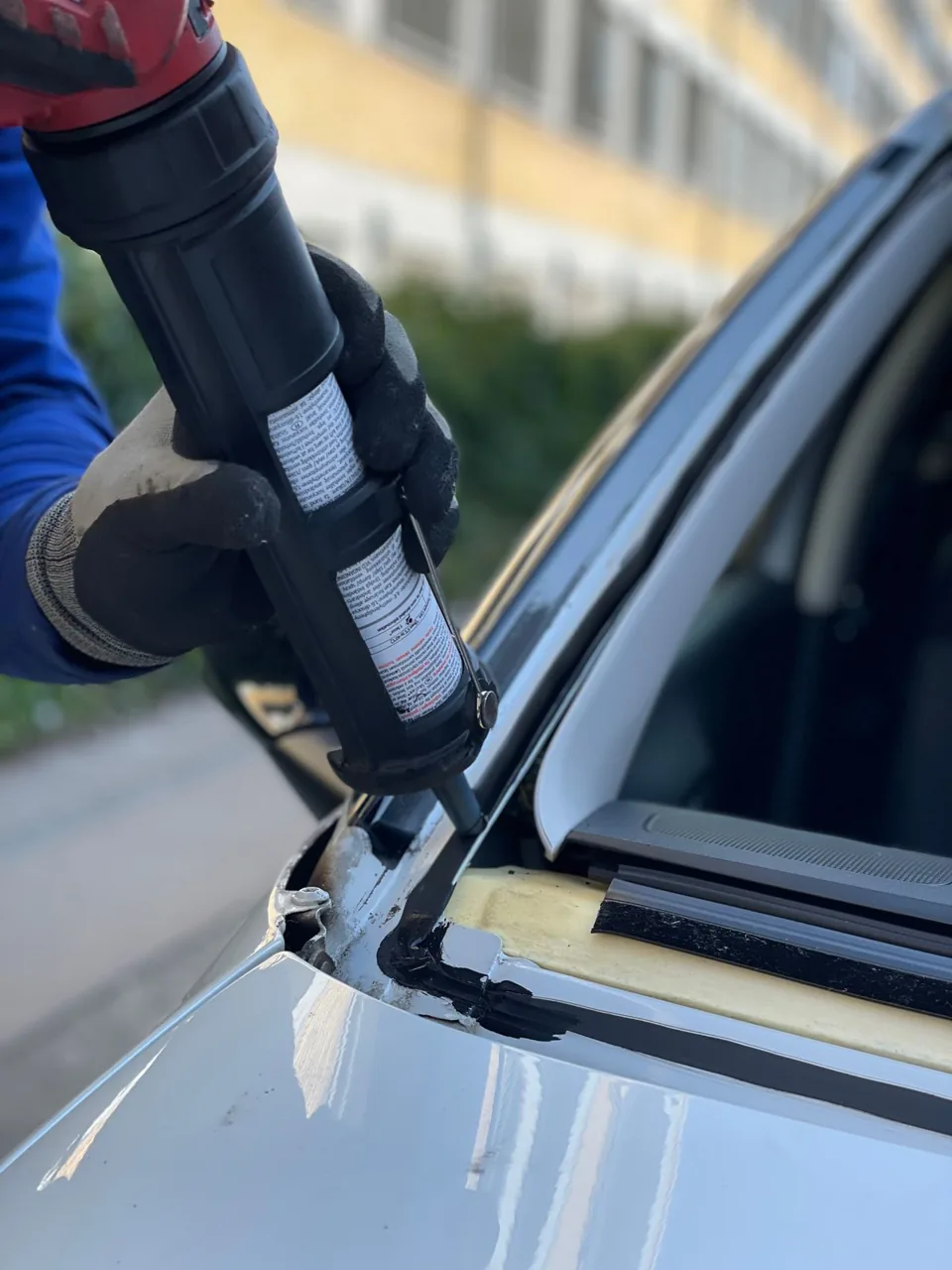 A gloved technician preparing a vehicle’s windshield opening for replacement